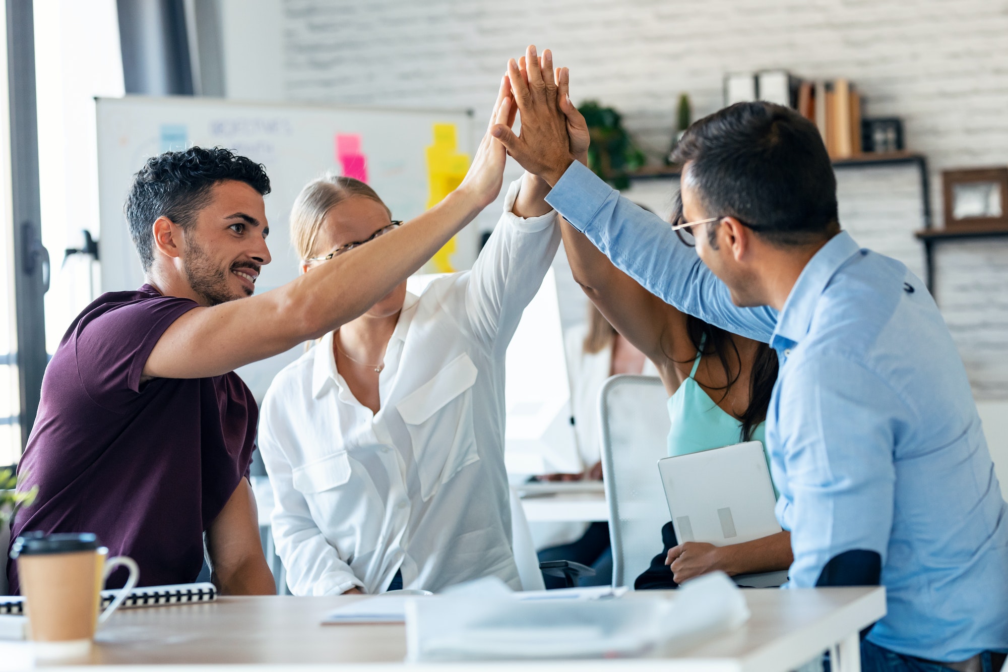successful-business-team-celebrating-good-job-while-holding-up-their-right-hands-on-coworking-place-.jpg